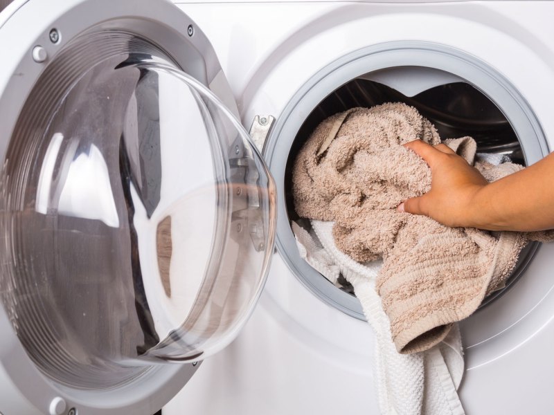 Hand gibt Handtücher in Waschmaschine