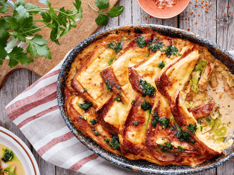 Brotauflauf mit Käse und Geschnetzeltem in einer dunklen Auflaufform.