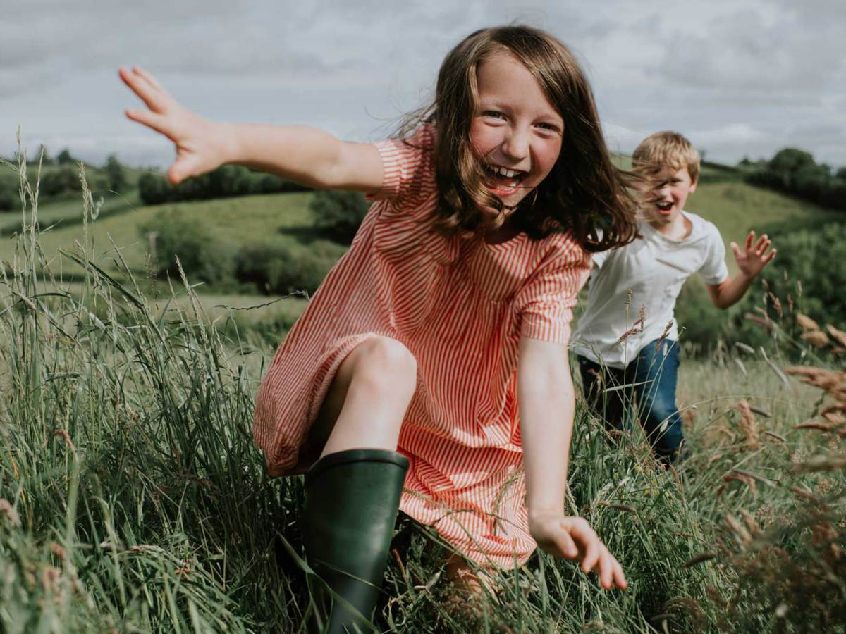 Zwei Kinder rennen im Sommer &uuml;ber ein Feld auf die Kamera zu.