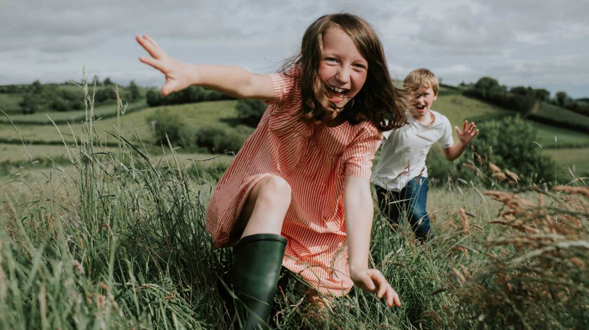 Zwei Kinder rennen im Sommer über ein Feld auf die Kamera zu.