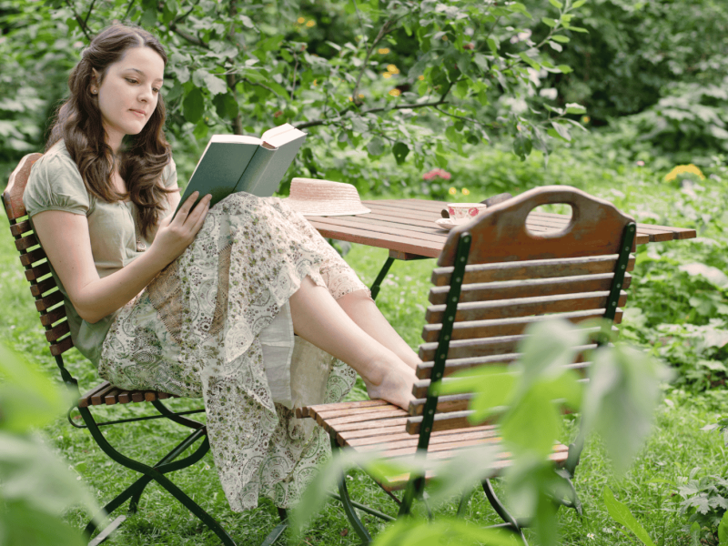Frau sitzt in ihrem Garten und liest ein Buch.