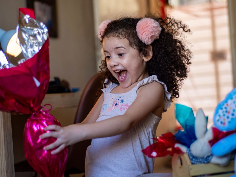 M&auml;dchen h&auml;lt ein buntes gro&szlig;es Ostergeschenk in der Hand und freut sich sehr,