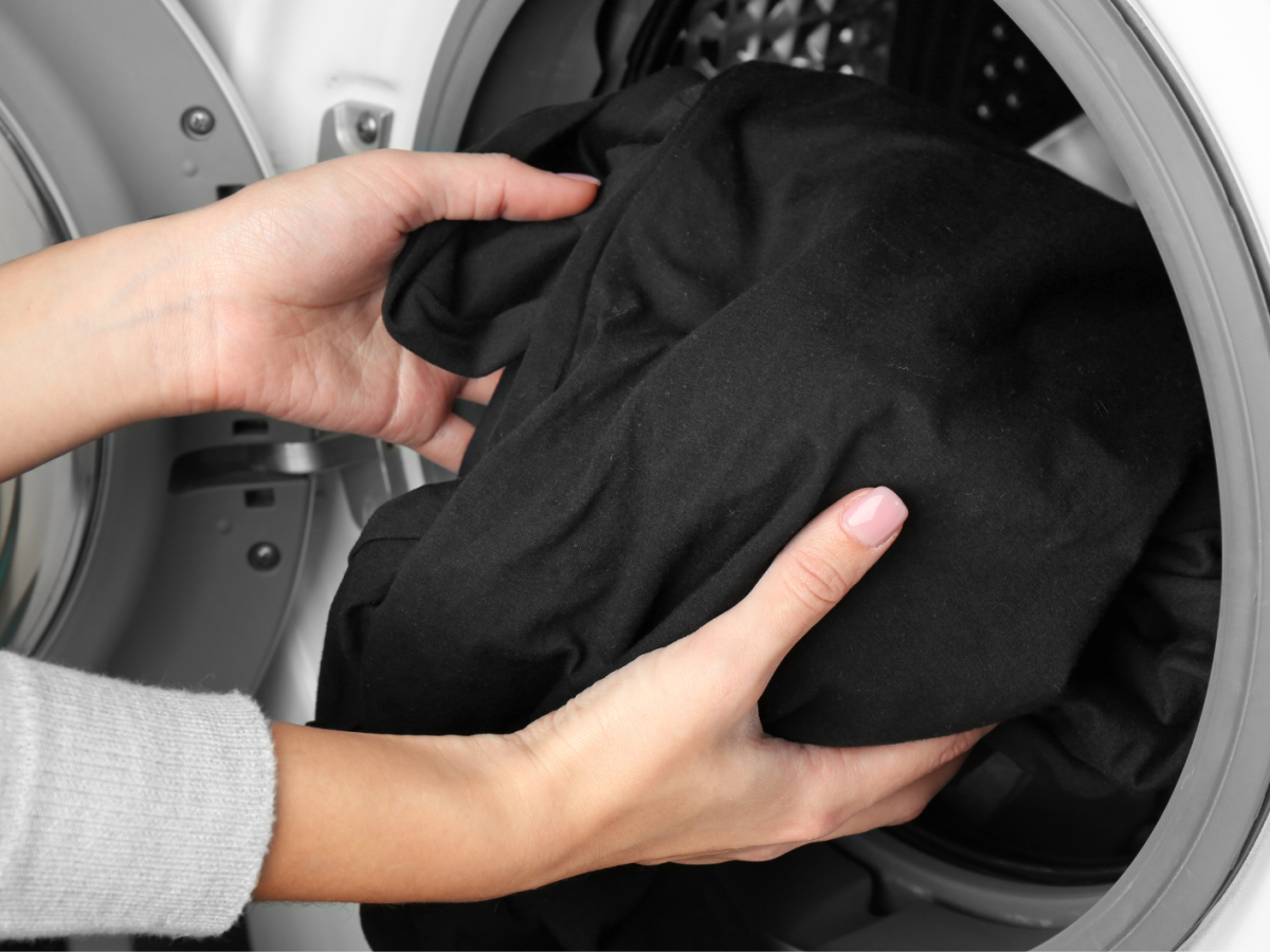 Frauenh&auml;nde geben ein schwarzes Kleidungsst&uuml;ck in die Waschmaschine