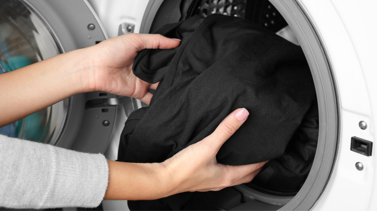 Frauenhände geben ein schwarzes Kleidungsstück in die Waschmaschine