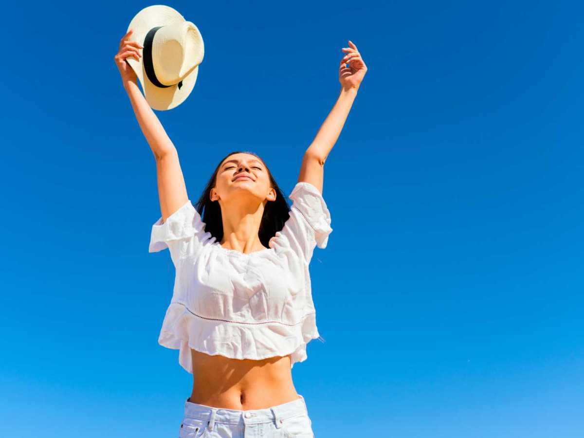 Frau streckt die Arme aus. Hinter ihr ist ein strahlend blauer HImmel.