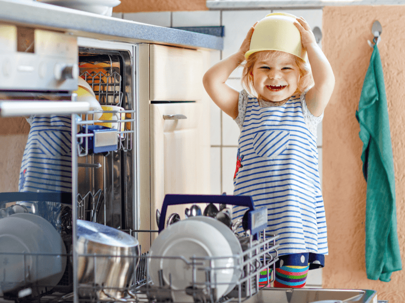 Kleines Kind steht vor geöffneter Spülmaschine.