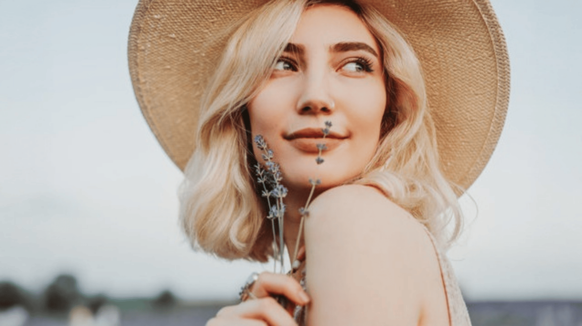 Junge Frau mit blonden Haaren hält Lavendel vor ihr Gesicht.