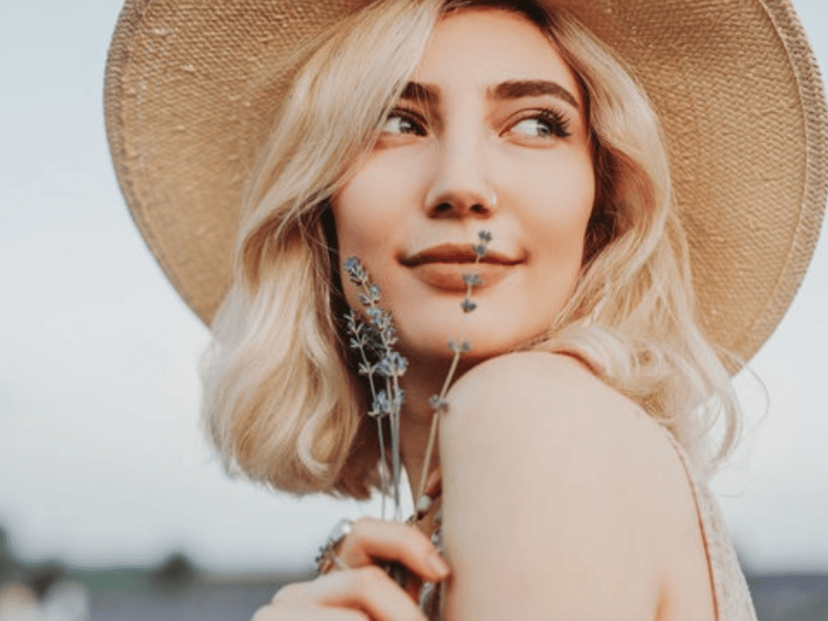 Junge Frau mit blonden Haaren hält Lavendel vor ihr Gesicht.