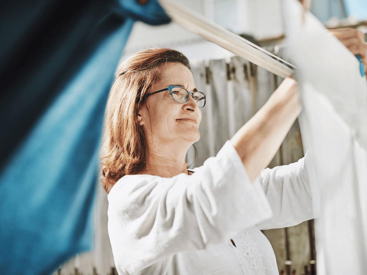 Frau h&auml;ngt W&auml;sche auf Leine im Garten auf.