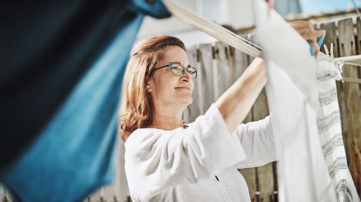 Frau hängt Wäsche auf Leine im Garten auf.