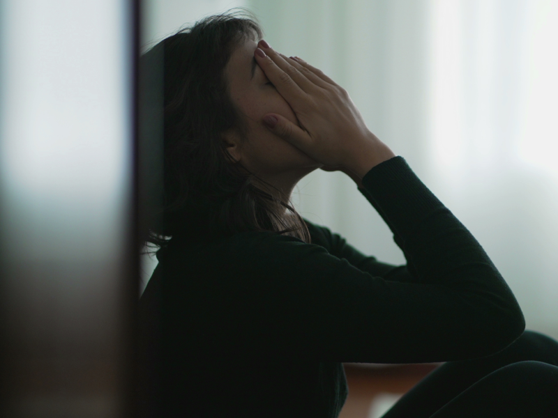 Frau sitzt traurig auf dem Boden mit den Händen vor dem Gesicht