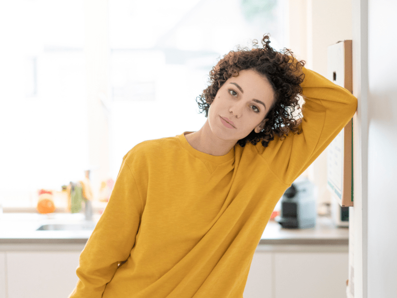 Frau mit dunklen Locken und einem gelben Pullover schaut ernst