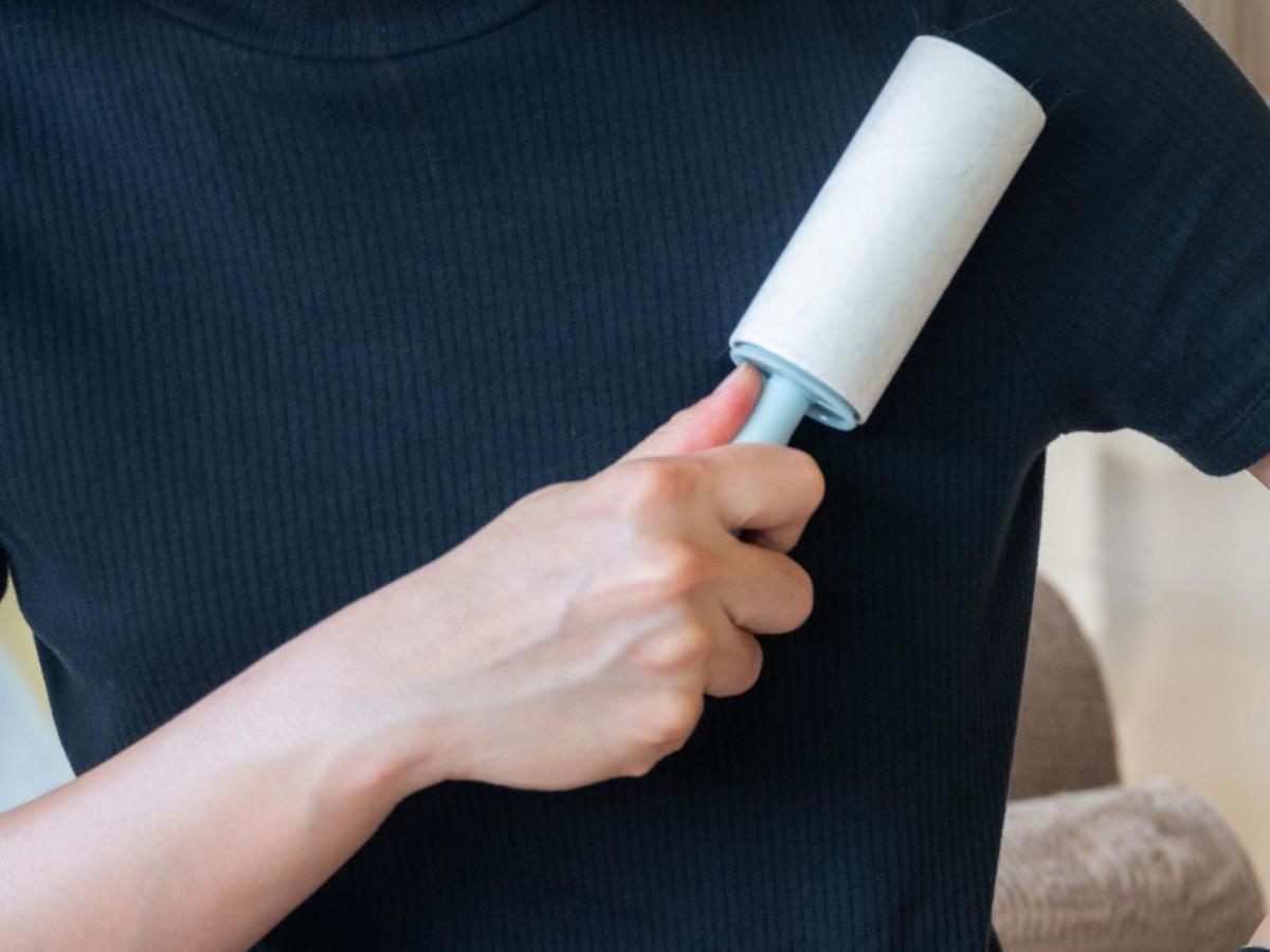 Frau mit einem dunklen T-Shirt streicht mit einer Fusselrolle über die Kleidung.