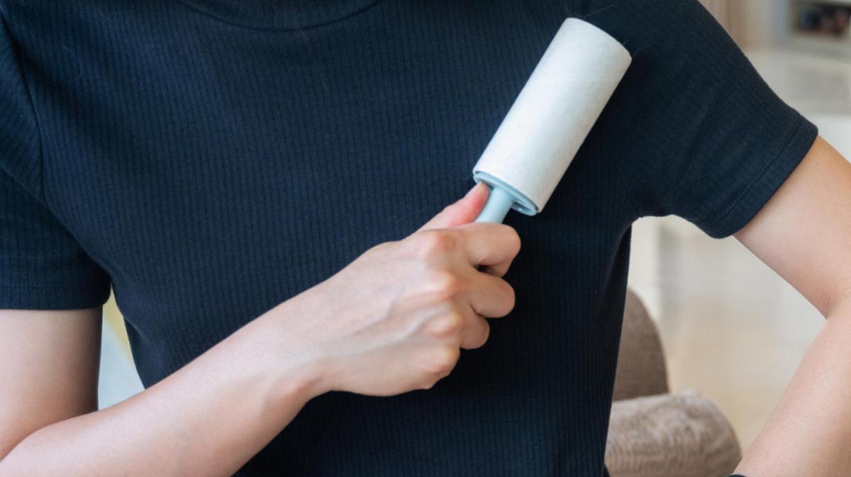 Frau mit einem dunklen T-Shirt streicht mit einer Fusselrolle über die Kleidung.