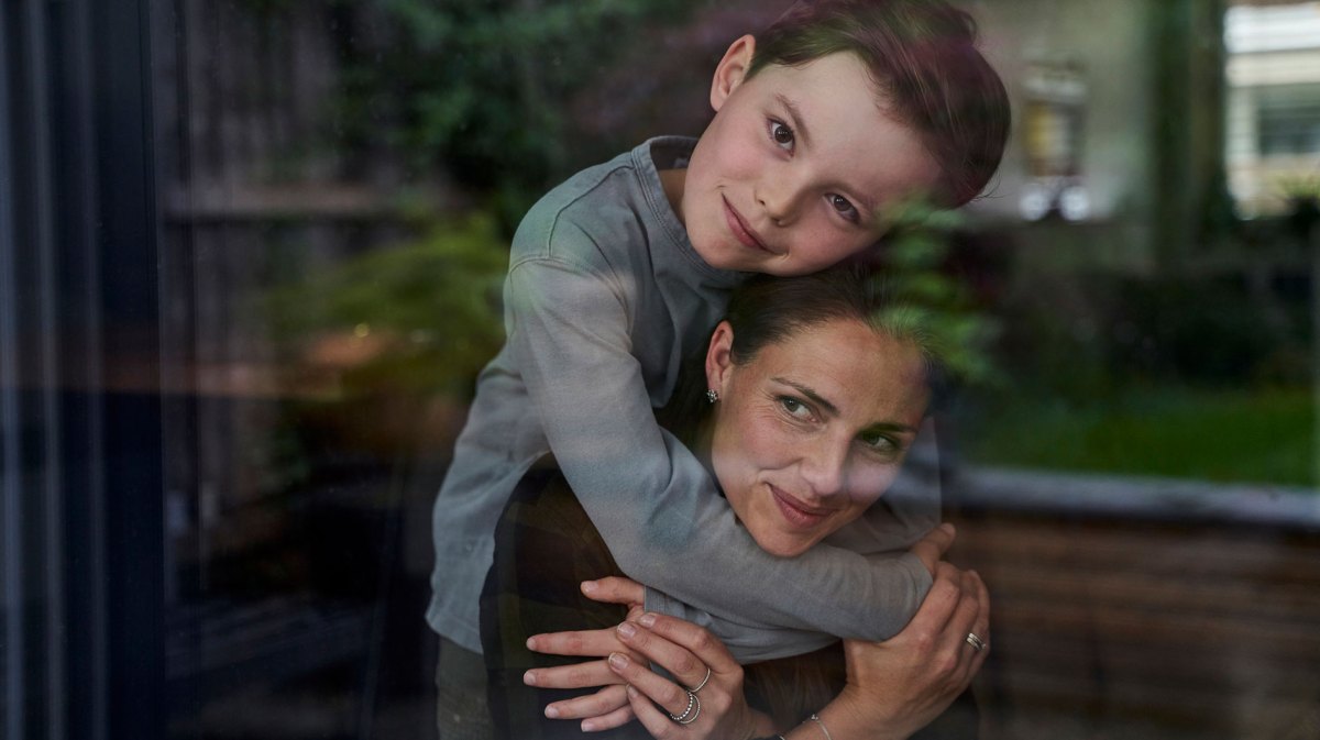 Kind umarmt die Mutter von hinten
