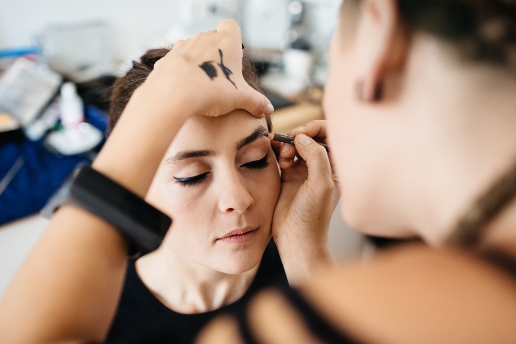Frau, die die Augenbrauen einer anderen Frau schminkt.