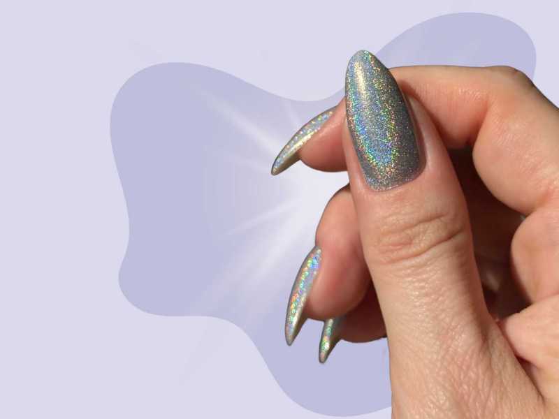Holografische Nägel in einem grauen Farbton vor einem lilafarbenen Hintergrund
