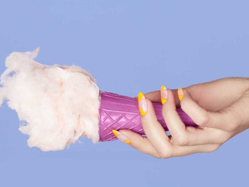 Hand mit gelb lackierten Fingernägeln hält ein Eis fest