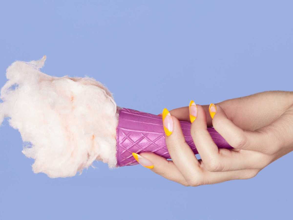 Hand mit gelb lackierten Fingernägeln hält ein Eis fest