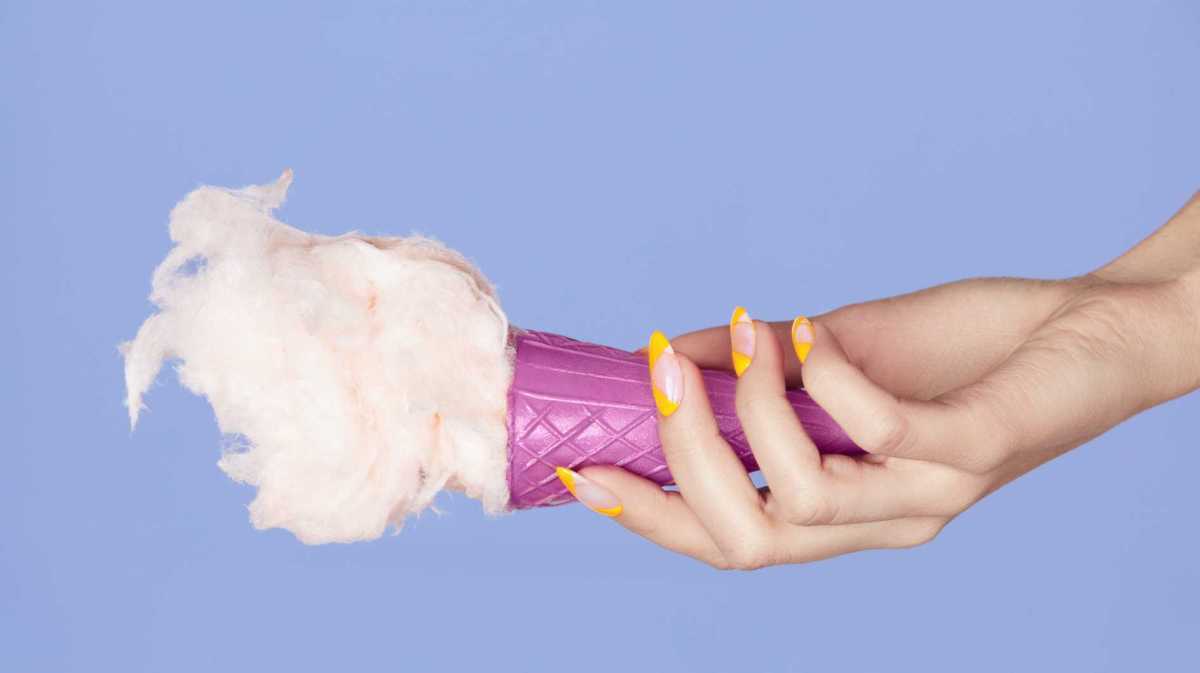 Hand mit gelb lackierten Fingernägeln hält ein Eis fest