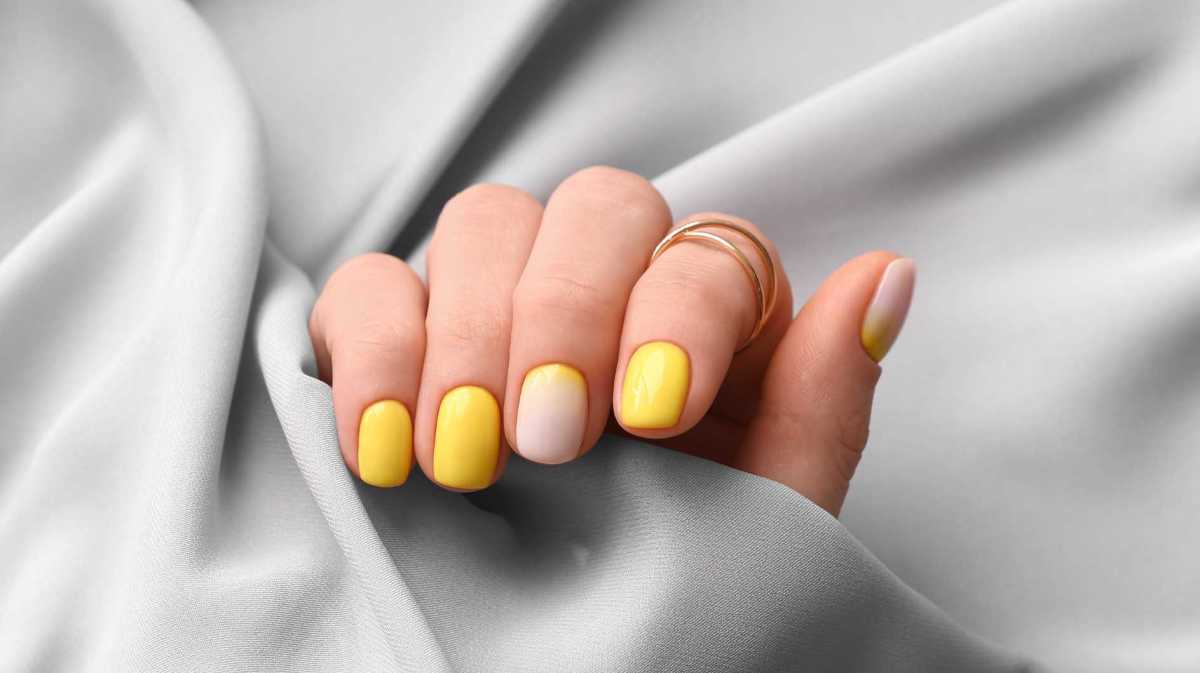 Gelb lackierte Fingernägel vor einem grauen Seidentuch