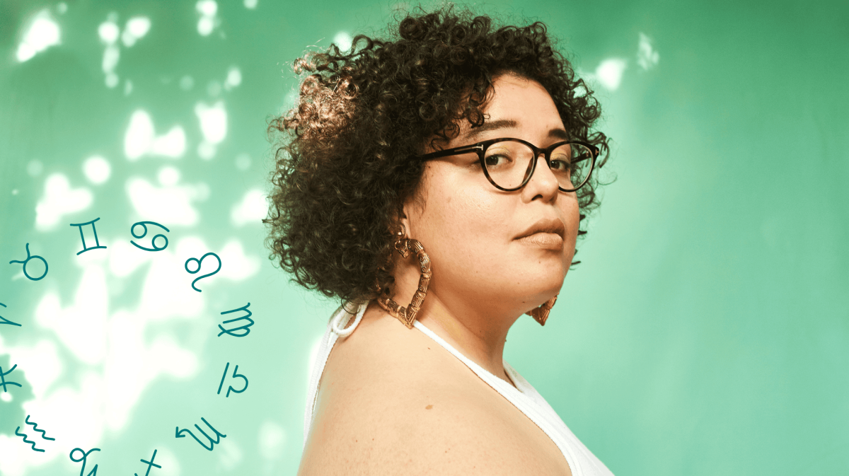 Frau mit Brille steht vor einem hellgrünen Hintergrund und guckt skeptisch in die Kamera.
