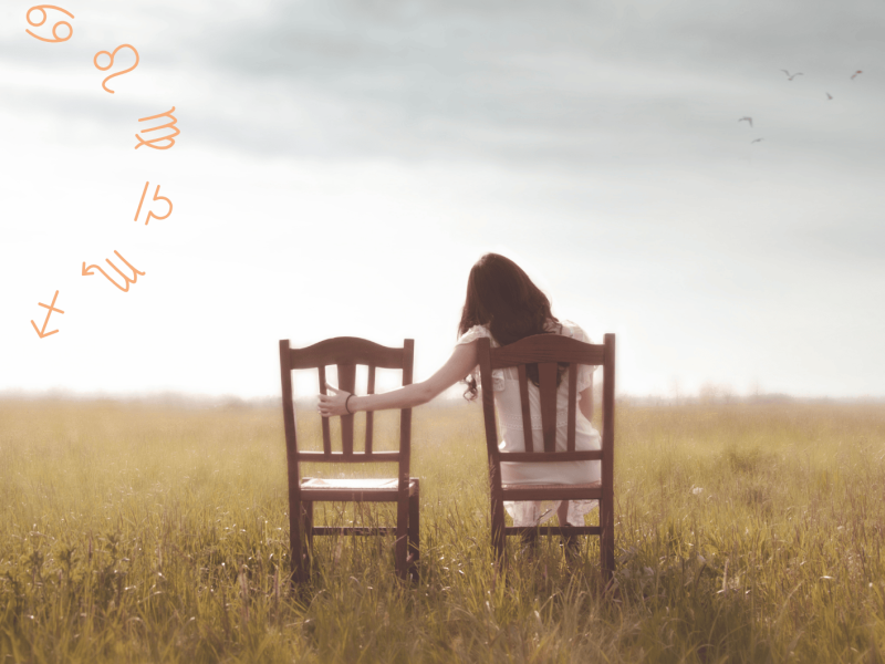 Frau sitzt auf dem Feld auf einem Stuhl und hält Hand auf leeren Stuhl neben ihr