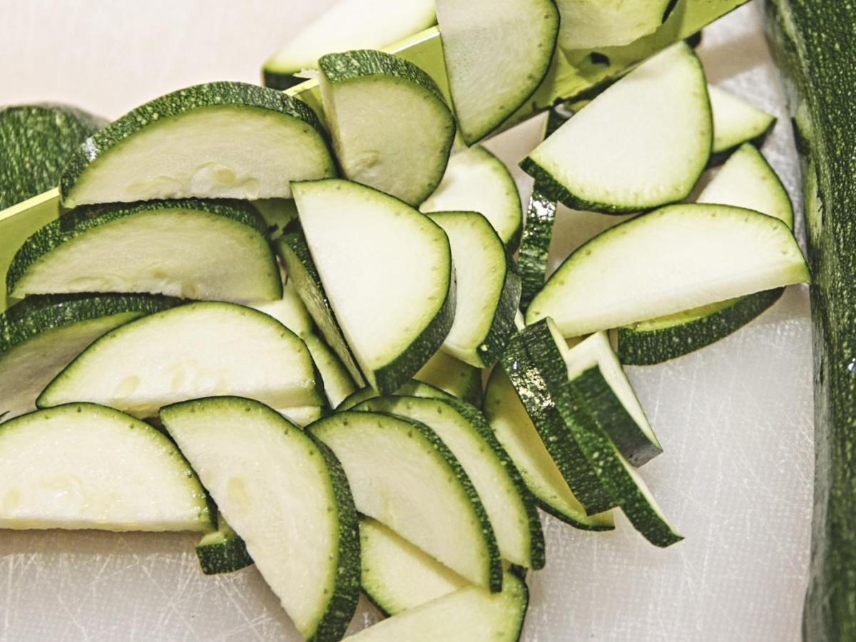 Geschnittene rohe Zucchini liegt auf einem Brett mit einem Messer.