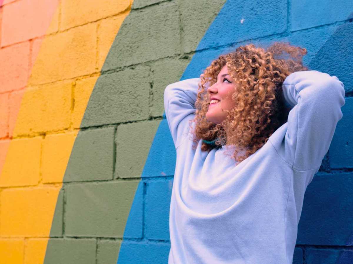 Junge Frau lehnt sich an eine bunte Wand.