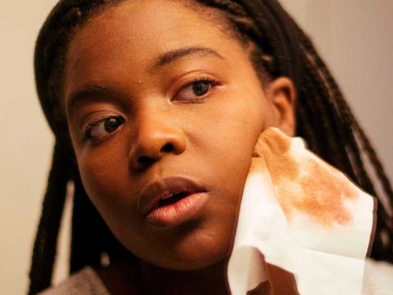 Junge Frau schminkt sich vor dem Spiegel ab.