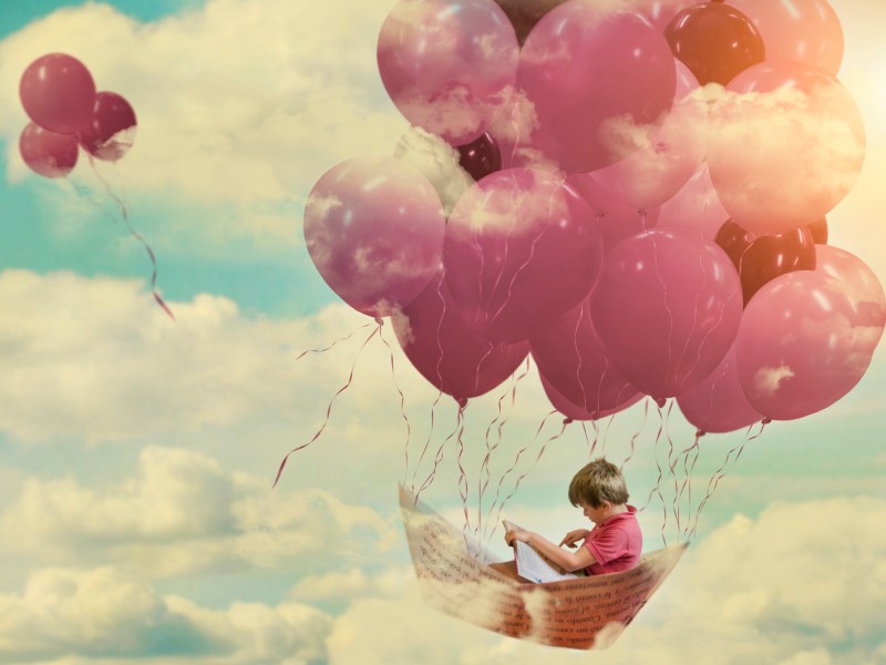 Kleiner Junge sitzt in einem Boot und schwebt auf Luftballons durch die Wolken