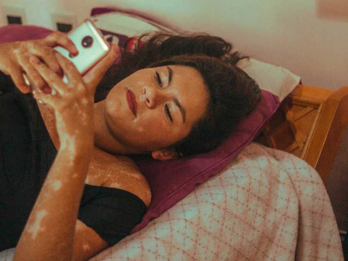 Junge Frau liegt auf ihrem Bett und benutzt ihr Handy.