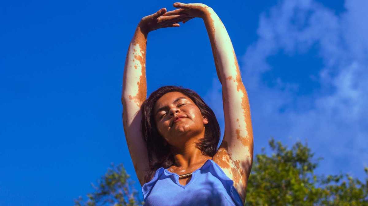Frau mit ausgestreckten Armen und blauem Himmel im Hintergrund.