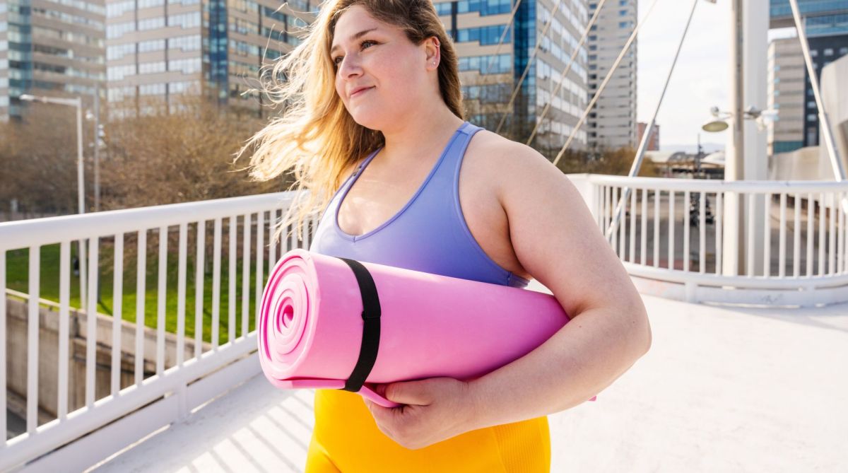 Frau mit Sportkleidung und pinker Sportmatte unter dem Arm draußen