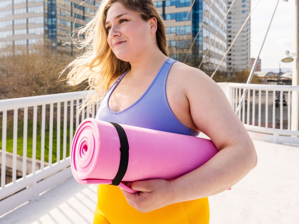 Frau mit Sportkleidung und pinker Sportmatte unter dem Arm draußen