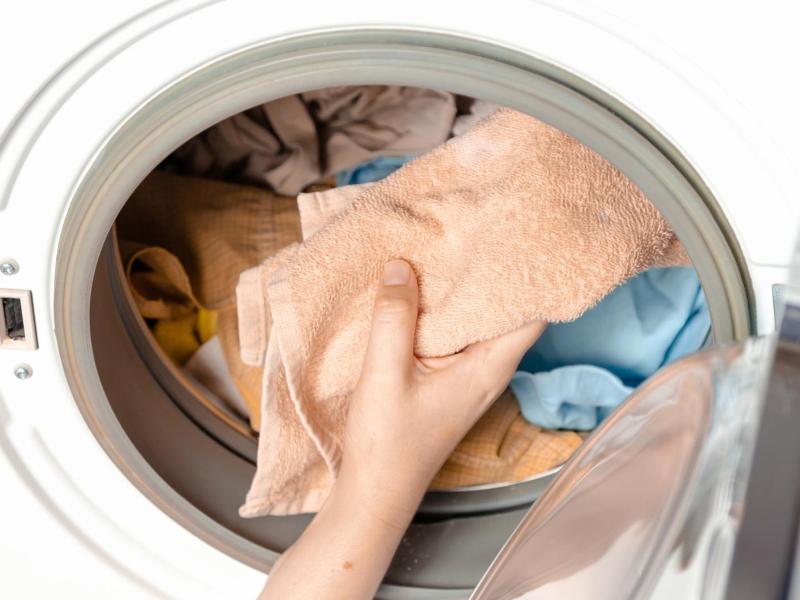 Eine Hand gibt Handtücher in eine Waschmaschine.