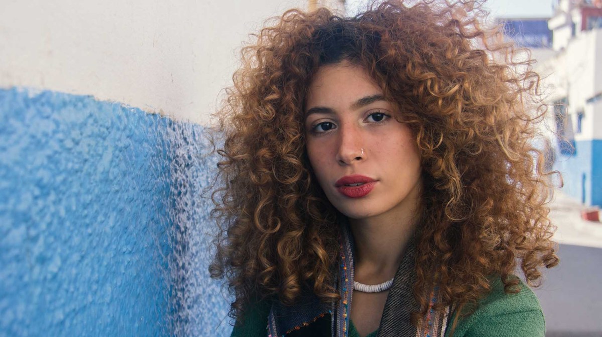 Frau mit Locken steht in einer Straße und schaut in die Kamera.