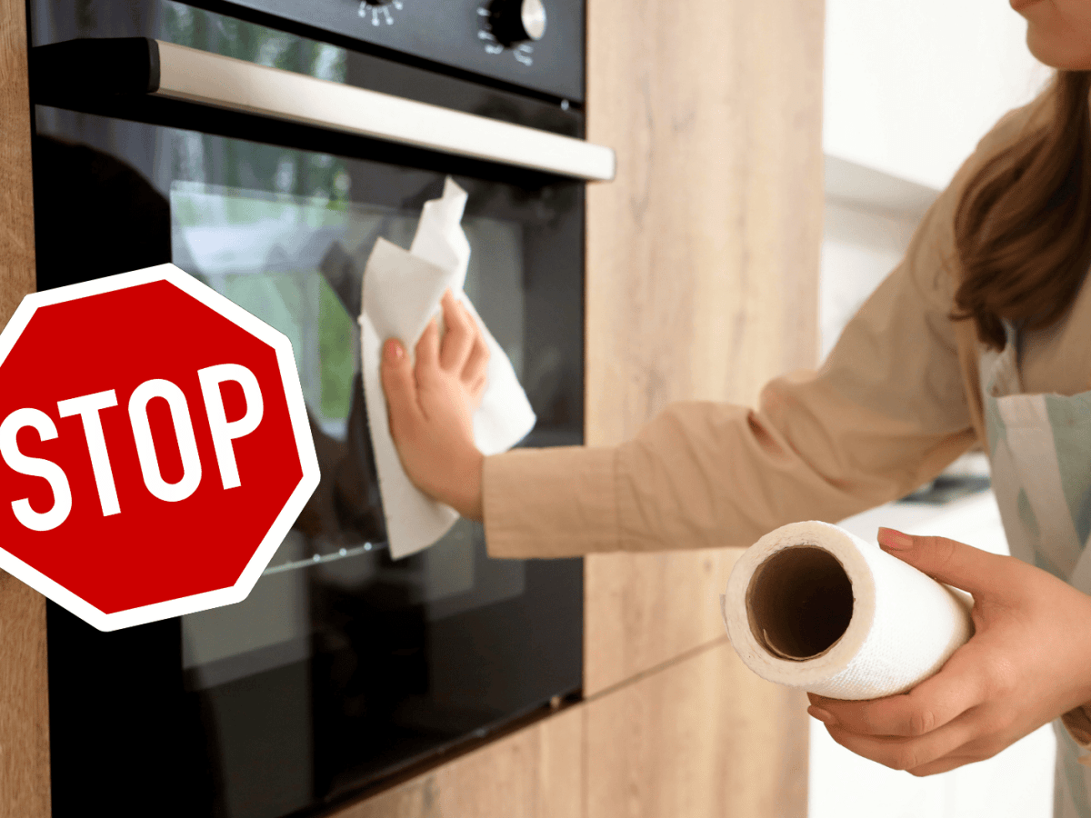 Frau wischt &uuml;ber Ofen mit K&uuml;chenrolle.