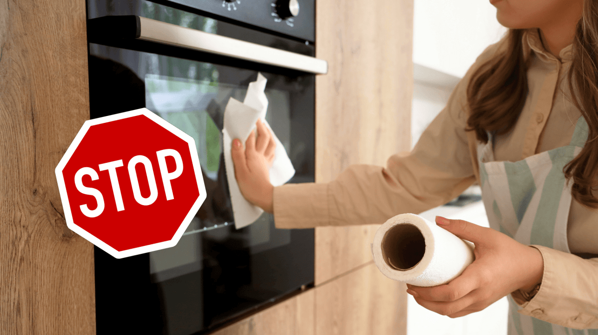 Frau wischt über Ofen mit Küchenrolle.