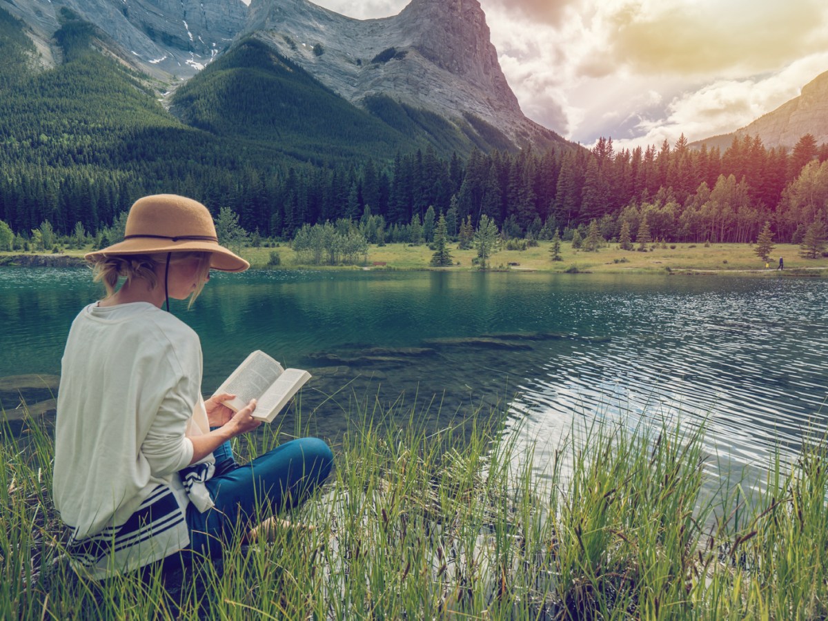 Frau liest ein Buch, im Hintergrund traumhafte Berge und See
