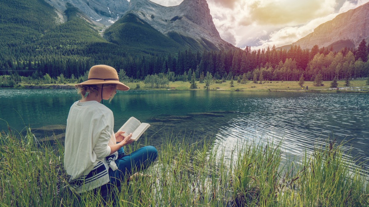 Frau liest ein Buch, im Hintergrund traumhafte Berge und See
