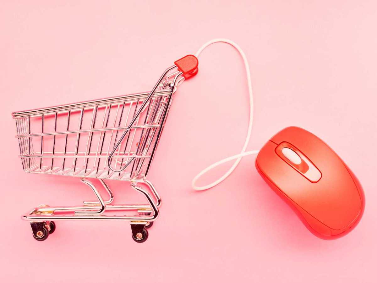 Einkaufswagen und rote Computermaus auf rosa Hintergrund.