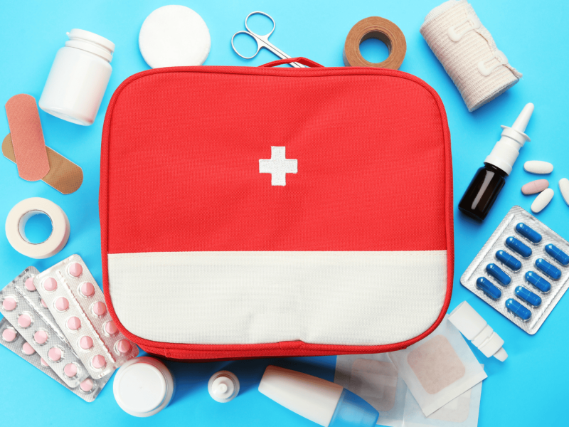 Medizinkästchen auf blauem Untergrund, darum liegen Tabletten, Mullbinden etc.