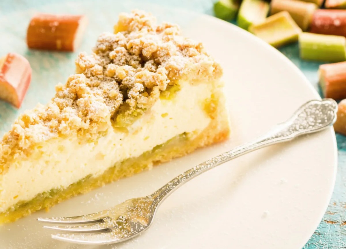 Käsekuchen mit Streuseln und Rhabarber auf weißem Teller.