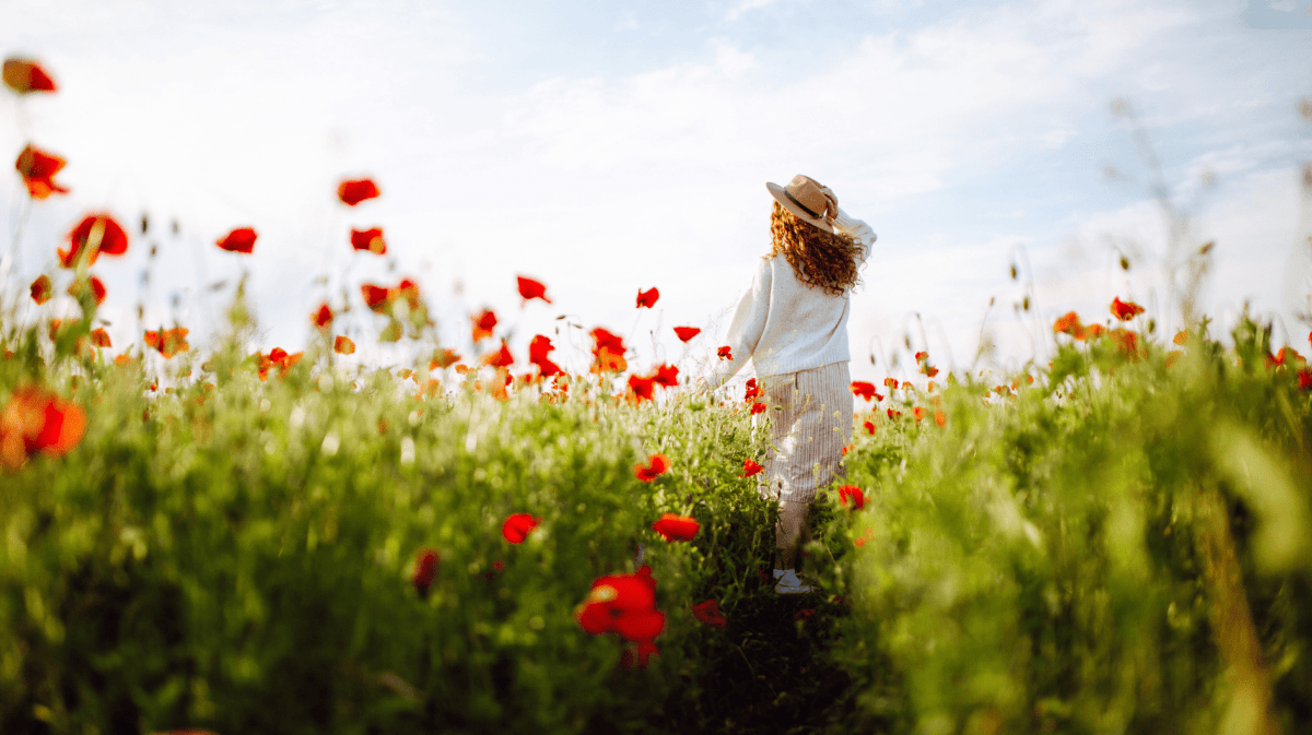 Frau mit roten Haaren läuft durch ein Feld mit Klatschmohn.