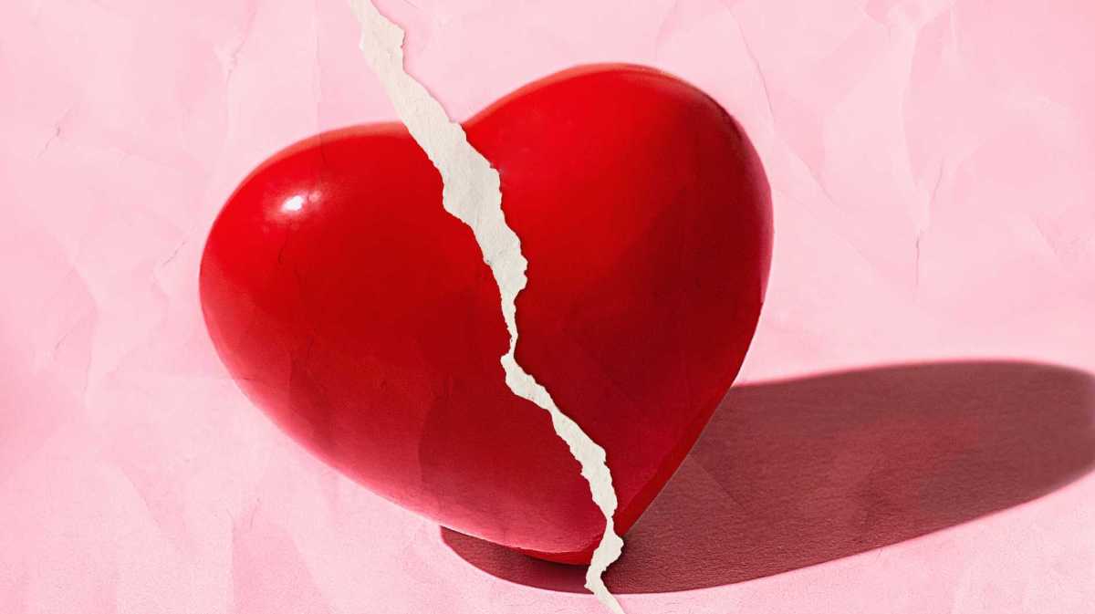 Rotes gebrochenes Herz auf pastellrosa Farbe mit zerrissenem Papiereffekt.