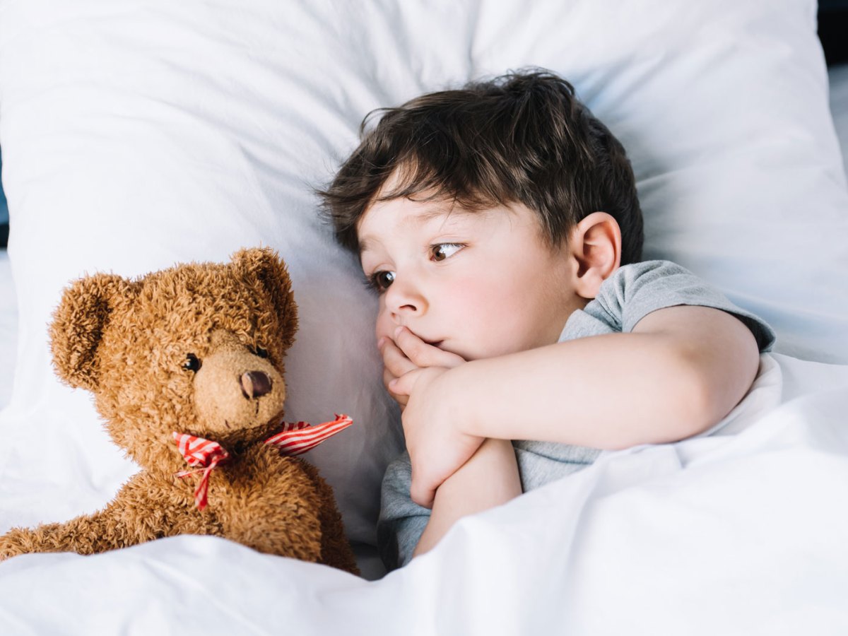Kleines Kind liegt im Bett und schaut seinen Pl&uuml;schteddy an, der neben ihm liegt.