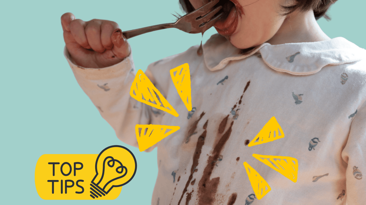 Kind isst mit einer Gabel Schokoladensoße und kleckert auf die Bluse, Fokus mit gelben Zeichen auf die Flecken.