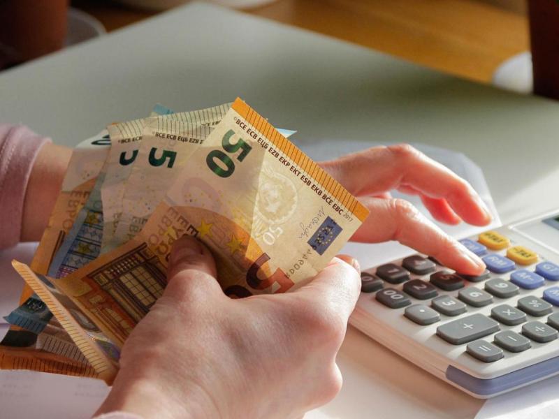 Frau hält Geldscheine in der Hand und tippt auf einem Taschenrechner.