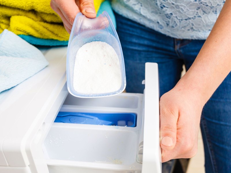 Frau füllt Waschpulver in Waschmaschine